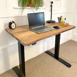 May include: A black standing desk with a wooden top and black metal legs. A laptop, a lamp, and a clock are on the desk.