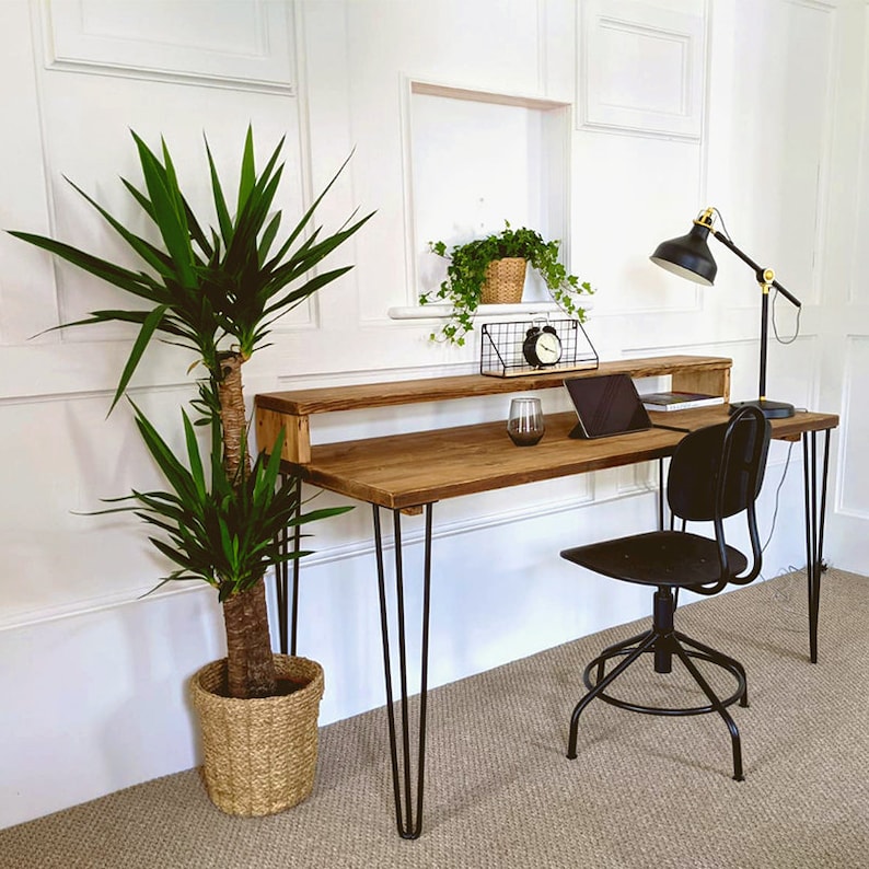 May include: A rustic wooden desk with a black metal frame and hairpin legs. The desk has a shelf above the main surface and is decorated with a potted plant, a lamp, and a laptop.