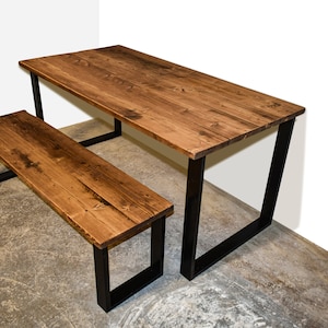 Könnte beinhalten: Ein rustikaler Holztisch und eine Holzbank mit schwarzen Metallbeinen. Tisch und Bank haben eine natürliche Holzoptik.