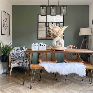May include: A dining room scene with a wooden table, bench, and chairs. A white fur throw is on the bench. A white vase with dried flowers sits on the table. Two boxes with the text "Lick" are on the table. A black framed mirror is on the wall.