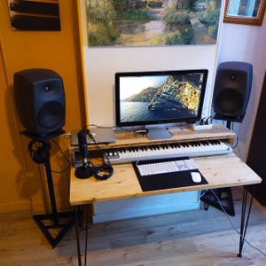 May include: A wooden desk with a black keyboard, a white keyboard, a microphone, a computer monitor, and two black speakers. The desk has black hairpin legs.