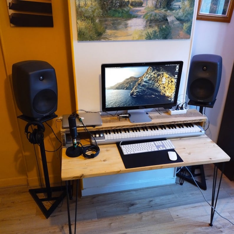 May include: A wooden desk with a black keyboard, a white keyboard, a microphone, a computer monitor, and two black speakers. The desk has black hairpin legs.