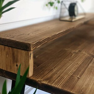 May include: A rustic wooden desk with a built-in shelf. The desk is made of reclaimed wood and has a natural finish. The shelf is ideal for storing books, plants, or other items.