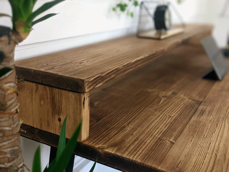 May include: A rustic wooden desk with a built-in shelf. The desk is made of reclaimed wood and has a natural finish. The shelf is ideal for storing books, plants, or other items.