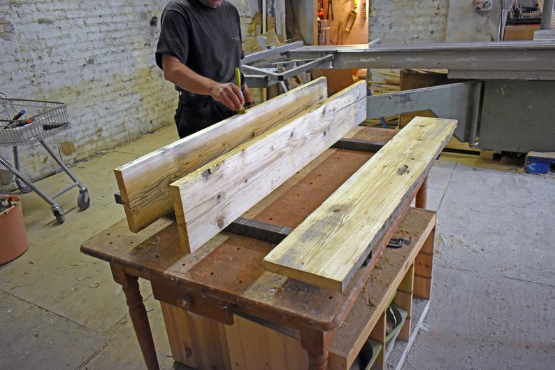 May include: Two long, light brown wooden planks are being measured and prepared for woodworking. The planks are resting on a workbench with a metal clamp holding them in place.
