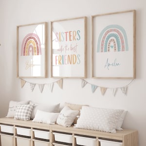 May include: Three framed prints featuring rainbow designs. The central print displays the text "SISTERS make the best FRIENDS". The left print shows a rainbow with the name "Bella" and the right print depicts a rainbow with the name "Amelia".