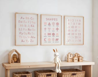 May include: Three framed educational prints with the alphabet, shapes, and numbers 0-30 in pink. A wooden shelf displays a wooden house, a stuffed bunny, and small wooden houses. Wicker baskets are below the shelf.