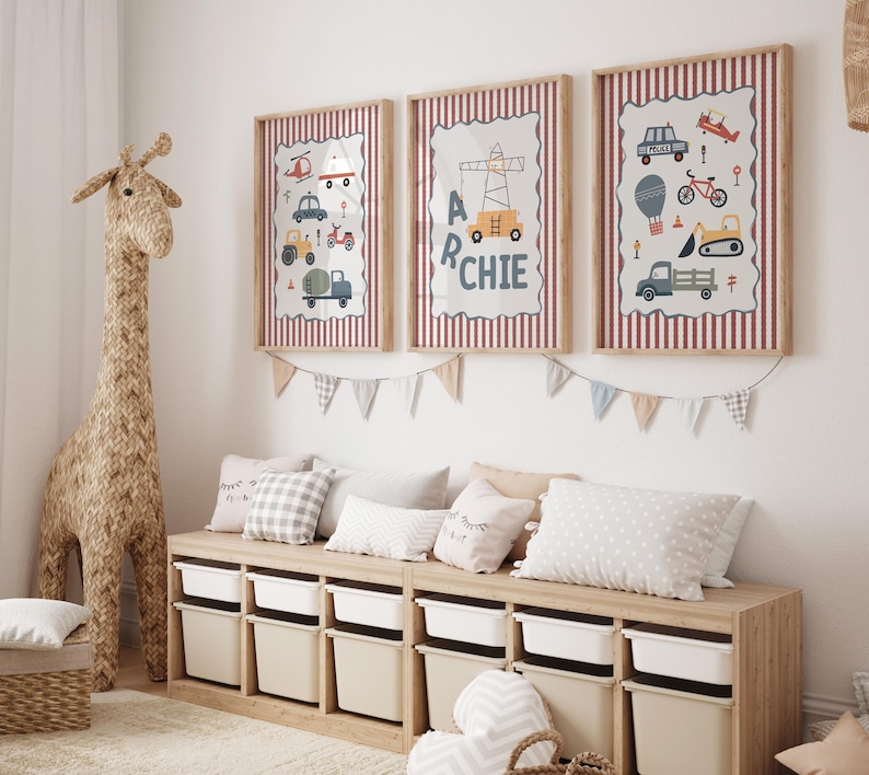 May include: Three framed wall prints featuring illustrations of construction vehicles, a police car, and a bicycle, with the name ARCHIE displayed on the center print. The prints have a red and white striped border and are hung above a wooden toy storage unit.