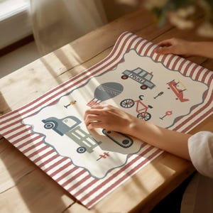 May include: A rectangular placemat featuring a cream-colored center with a scalloped border and red and white striped edges. The center displays illustrations of a police car with the text POLICE, a hot air balloon, a bicycle, and a tractor.