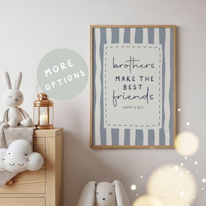 Könnte beinhalten: Ein gerahmter Druck mit dem Text "brothers make the best friends" in handschriftlichem Stil. Der Hintergrund hat vertikale blaue und weiße Streifen. Ein Plüschhase, ein Wolkenkissen und eine Kerzenlaterne befinden sich auf einer Holzkommode.