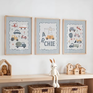 May include: Three framed wall art prints featuring light blue and white vertical stripes. The prints display illustrations of various construction vehicles, a crane, and the name ARCHIE in dark gray lettering, all set within light gray borders.