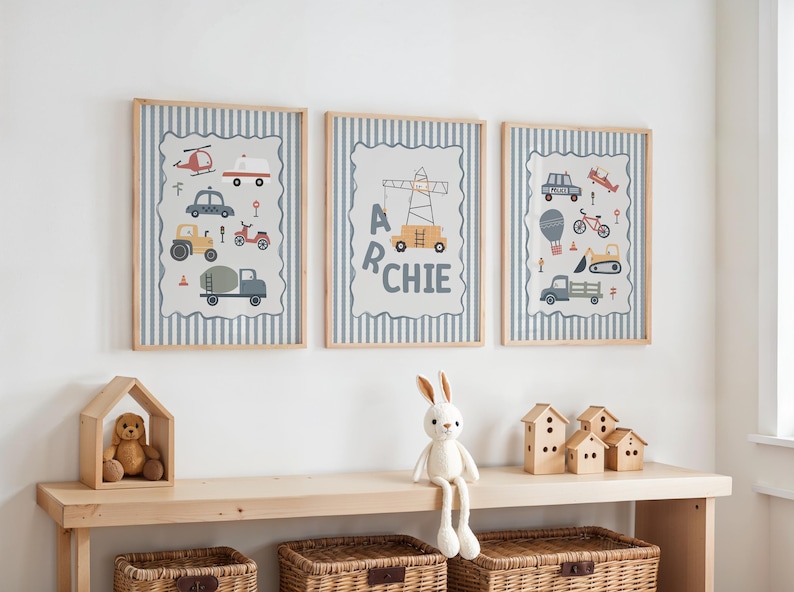 May include: Three framed wall art prints featuring light blue and white vertical stripes. The prints display illustrations of various construction vehicles, a crane, and the name ARCHIE in dark gray lettering, all set within light gray borders.