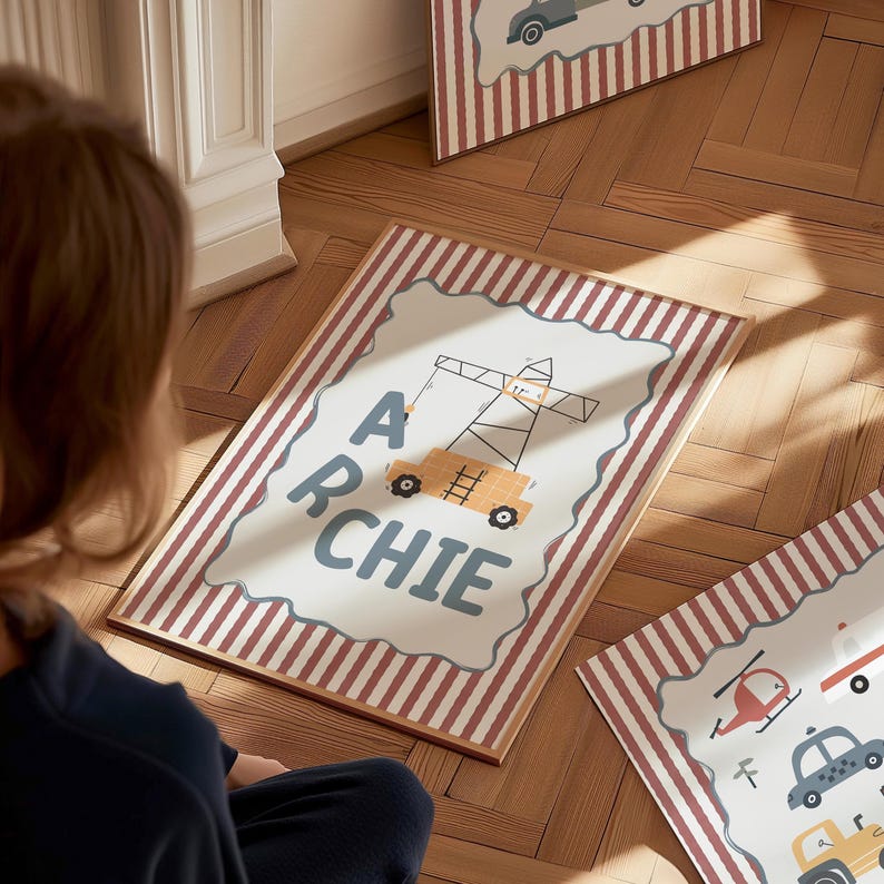 May include: A rectangular framed print featuring a white center with a scalloped edge, displaying the name ARCHIE in dark blue letters alongside a yellow construction crane illustration. The border has vertical red and white stripes.