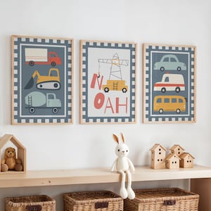 May include: Three framed prints with colorful illustrations of vehicles, including a truck, excavator, cement mixer, car, ambulance, and school bus. The middle print has the name "NOAH". The prints are displayed above a wooden shelf with toys.