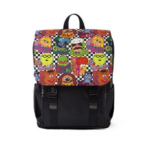 May include: Black backpack with a flap closure and adjustable straps. The top flap features a colorful pattern of Muppet characters on a checkered background. The backpack has a black handle and a front pocket.
