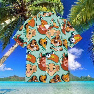 Puede incluir: Una camisa de manga corta con un patrón repetido de caras de personajes de dibujos animados en tonos naranja, beige y marrón sobre un fondo verde azulado claro. La camisa tiene un cuello clásico y botones. El fondo muestra una escena de playa tropical.