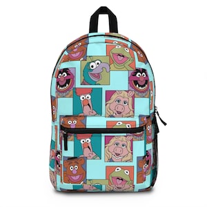 May include: A light blue backpack featuring a repeating pattern of Muppet characters in colorful squares. The backpack has a black top handle, black zippers, and a black mesh side pocket. The design includes characters like Kermit, Miss Piggy, and Fozzie Bear.