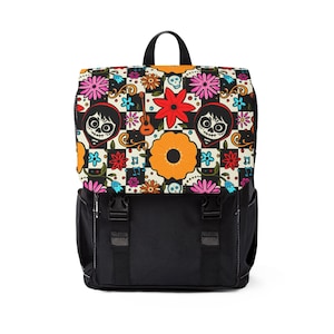 May include: A black backpack with a colourful flap featuring a Day of the Dead design. The flap has a chequered pattern with sugar skulls, flowers, and musical notes. The backpack has two black straps and a top handle.