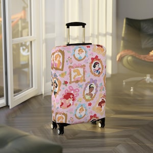May include: A pink suitcase cover with framed portraits of animated princesses. The cover has a repeating pattern of princess portraits, flowers, and bows. The suitcase has a black handle and wheels, and is on a wooden floor.