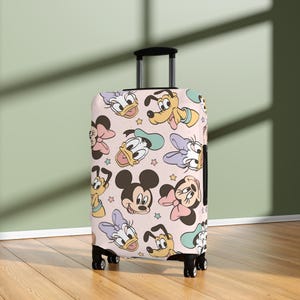 May include: A rolling suitcase featuring a pattern of cartoon character faces, including Mickey Mouse, Minnie Mouse, Donald Duck, and Goofy, on a light pink background. The suitcase has a black handle and wheels.