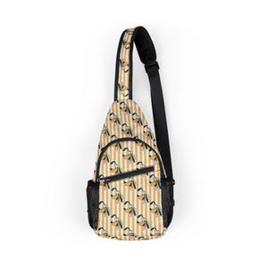 May include: A sling bag featuring a repeating pattern of Pluto's face on a cream and gold striped background. The bag has a black adjustable strap, a black mesh side pocket, and a black zipper.
