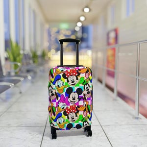 May include: A patterned rolling suitcase with cartoon characters such as Mickey and Minnie Mouse, Donald Duck, and Goofy. The suitcase has a black handle and wheels. The background is a blurred airport scene.
