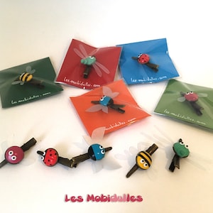 May include: Assortment of colorful insect hair clips packaged on individual cards. The insects include a ladybug, a bee, a dragonfly, and a fly. Each card features the text "Les Mobidulles.com".