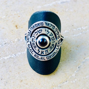 Puede incluir: Un anillo de plata con una piedra roja oscura en el centro. El anillo está inscrito con texto hebreo en un círculo alrededor de la piedra.