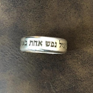 Puede incluir: Un anillo de plata con texto en hebreo que dice "לשם אהבה", que se traduce como "Por amor".