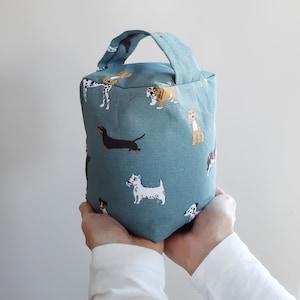 May include: A teal blue doorstop featuring a variety of dog breeds printed on it. The doorstop has a handle and is made of fabric.