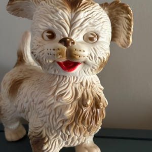 Peut inclure: Un chien en caoutchouc jouet vintage, blanc et brun, avec une bouche rouge et des yeux bruns. Le chien est debout sur ses quatre pattes et a une texture moelleuse.