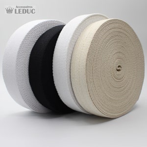 May include: Four rolls of woven webbing in white, black, off-white, and beige. The rolls are tightly wound, showing the texture of the material. The image is well-lit, highlighting the different colors and textures of the webbing.
