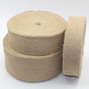 Peut inclure: Plusieurs rouleaux de ruban de jute de couleur naturelle sont empilés les uns sur les autres. Le ruban est tissé serré et a un aspect texturé. Les rouleaux sont de tailles variables, avec un debout pour montrer le bord.
