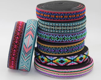 May include: A stack of colorful patterned elastic ribbons. The ribbons feature various geometric designs in shades of pink, blue, green, and orange. The ribbons are stacked on top of each other, with a few ribbons leaning against the stack.