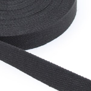 May include: A roll of black cotton webbing. The tightly woven fabric is a solid black color and appears to be unwound from a larger roll. The webbing is likely used for straps, belts, or other crafting projects.