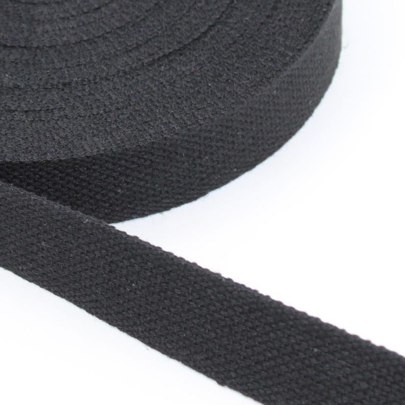 May include: A roll of black cotton webbing. The tightly woven fabric is a solid black color and appears to be unwound from a larger roll. The webbing is likely used for straps, belts, or other crafting projects.