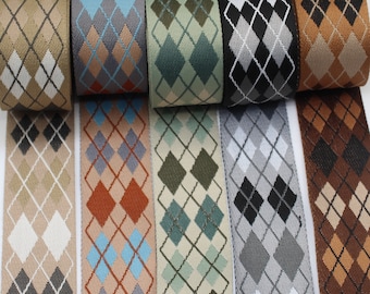 May include: Assortment of argyle patterned ribbons in various colors, including tan, gray, green, black, and brown. Each ribbon features a repeating diamond design. The ribbons are rolled up, showcasing the different color combinations and patterns.