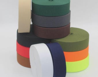 May include: A collection of elastic bands in various colors, including beige, green, gray, brown, black, red, white, navy blue, orange, and neon yellow. The bands are rolled into circular shapes, stacked and arranged to showcase the color variety.