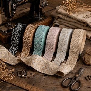 May include: A collection of six rolls of woven fabric ribbon featuring a repeating diamond pattern in black, brown, teal, pink, light blue, and beige. The ribbons are displayed alongside a vintage sewing machine, metal buckles, and scissors.