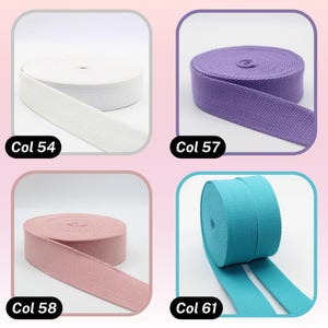 May include: Four spools of canvas webbing in various colors: white (Col 54), purple (Col 57), pink (Col 58), and turquoise (Col 61). Each spool is neatly rolled, with a portion of the webbing unrolled to show the texture. The text "Col" followed by a number is visible on each spool.