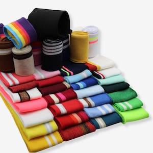 Könnte beinhalten: Eine Sammlung farbenfroher Armbänder und Schweißbänder in verschiedenen Farben und Designs. Das Sortiment umfasst Bänder mit Streifen, unifarbenen Designs und Regenbogenmustern. Die Armbänder sind gestapelt und gerollt, was eine Vielzahl von Stilen zeigt.