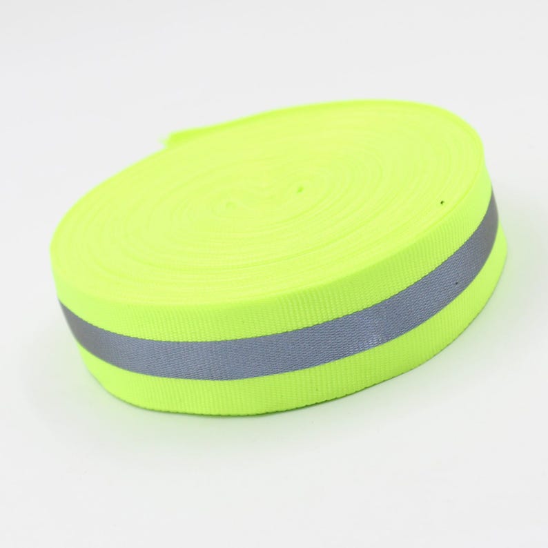 May include: A roll of bright neon yellow reflective tape with a gray reflective stripe. The tape is tightly wound, showing the edges of the fabric. The background is plain white.