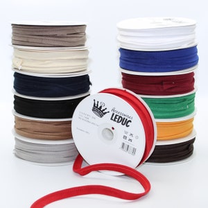 Könnte beinhalten: Ein Stapel Spulen mit verschiedenen farbigen Stoffbändern. Die Spulen sind mit "Accessoires LEDUC" beschriftet und haben ein Kronenlogo. Das Band ist aus Mikrofaser und besteht zu 100% aus Polyester.