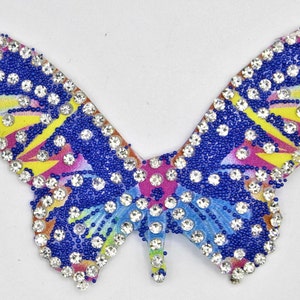 Peut inclure: Un patch en forme de papillon coloré avec des accents bleus, roses, jaunes et blancs. Le patch est recouvert de petits strass transparents.
