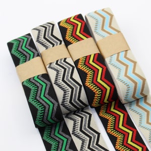 Op de afbeelding: Vier verschillende elastische banden met een zigzagpatroon in zwart, beige, rood en blauw. De banden hebben allemaal dezelfde breedte en een zigzagpatroon met verschillende kleuraccenten.