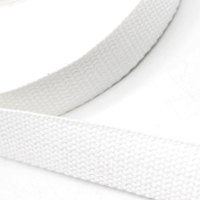 May include: Close-up of a white, woven fabric strap. The strap is thick and appears to be made of a durable material. The texture of the fabric is visible, with a slightly raised, ribbed pattern. The strap is likely used for crafting or sewing projects.