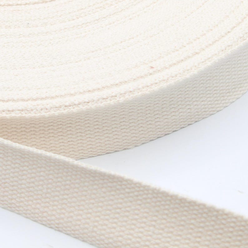 May include: A roll of natural-colored cotton webbing. The webbing is tightly woven and appears to be unwound from a larger roll. The color is a creamy off-white, and the texture is slightly ribbed.