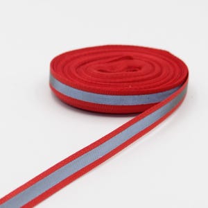 May include: A roll of red ribbon with a reflective silver stripe running down the center. The ribbon is neatly coiled, with a portion unraveled, displaying its full width. The background is plain white, highlighting the vibrant color of the ribbon.