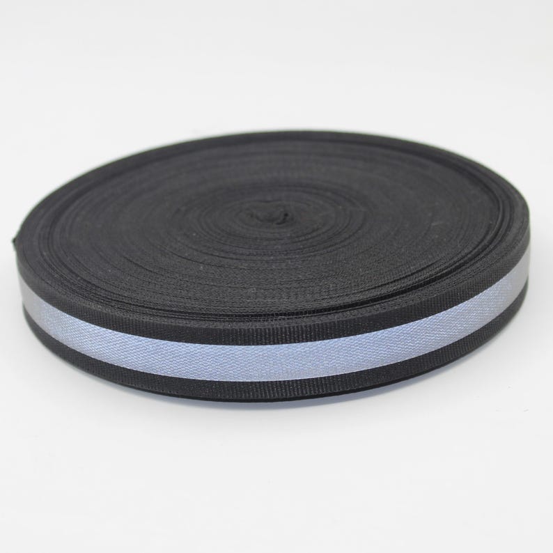 May include: A roll of black webbing with a reflective silver stripe running along the center. The webbing is tightly wound, showing the texture of the material. The reflective stripe adds a safety feature.
