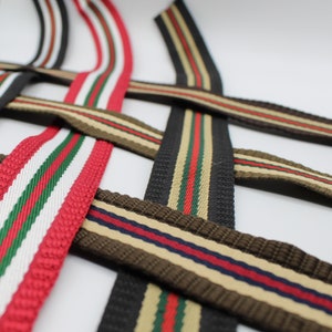 May include: Four different striped webbing straps in red, white, green, black, brown, and beige colours. The straps are woven with a textured pattern.